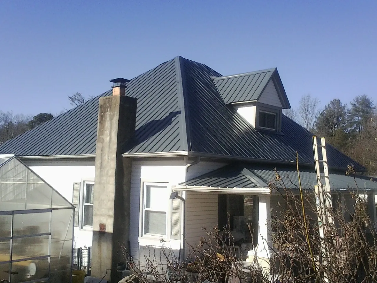 Dark blue standing seam metal roof on a white farmhouse with dormer — Slate & Tile Roof Repair by Roofing Brothers in Blue Rock