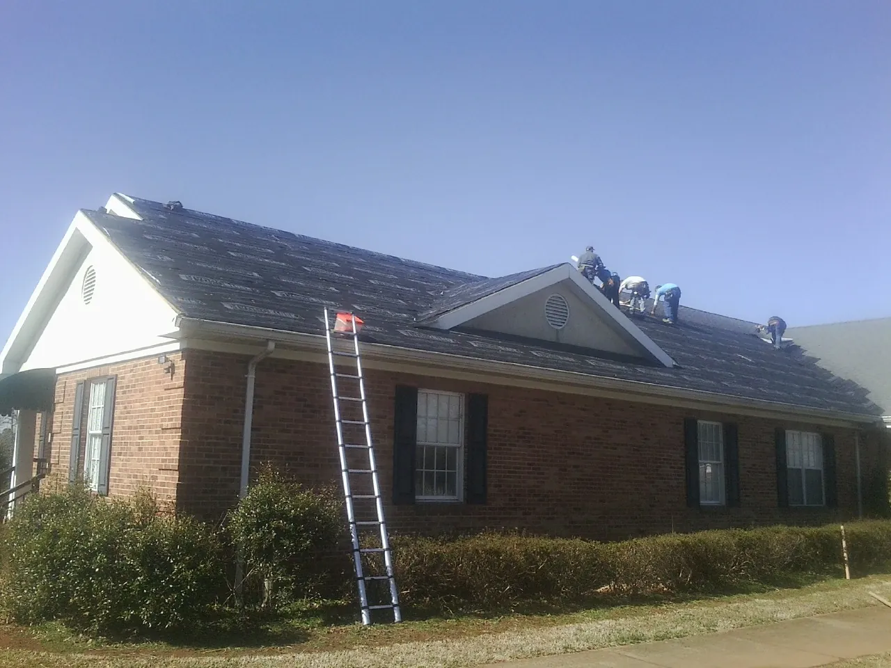 Crew tearing shingles off a brick ranch roof with a ladder set — Emergency Roof Repair work by our crew in Blue Rock