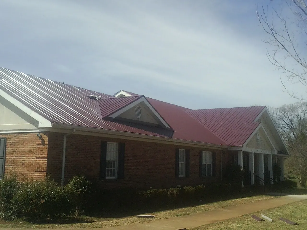 Red metal roof with gabled entries on a long brick building, from a Hail Damage Roof Repair job in Blue Rock
