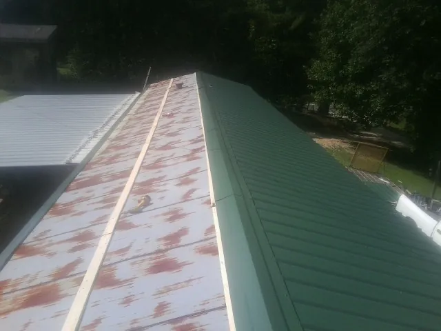 Old rusted panels beside newly installed green metal roofing — Wind Damage Roof Repair by Roofing Brothers in Blue Rock