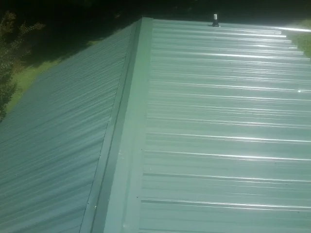 New green metal panels meeting at the ridge of a roof — Flat Roof Repair work by our crew in Blue Rock