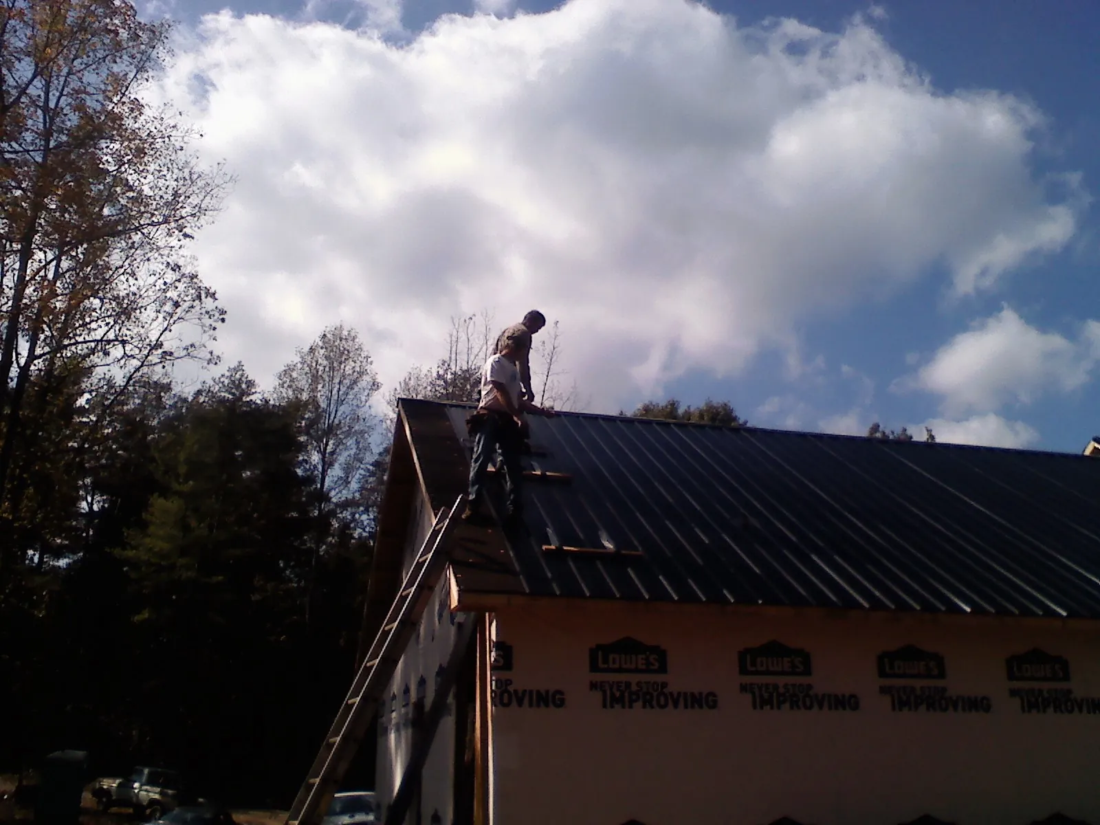 Roofer fastening dark metal panels high against a cloudy sky, from a Roof Inspection job in Blue Rock