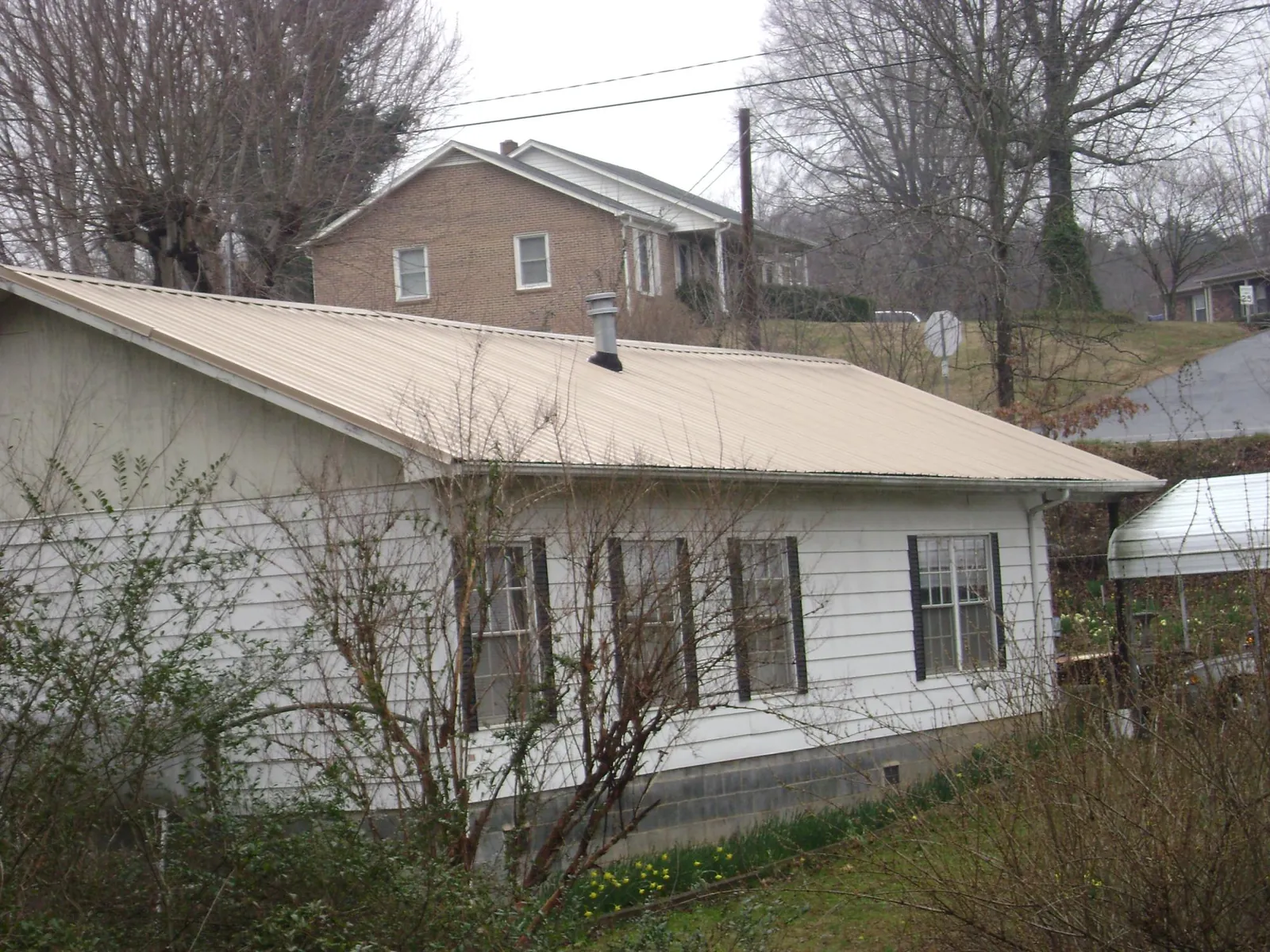 Tan metal roof on a white sided house set into a hillside — Commercial Roofing by Roofing Brothers in Blue Rock