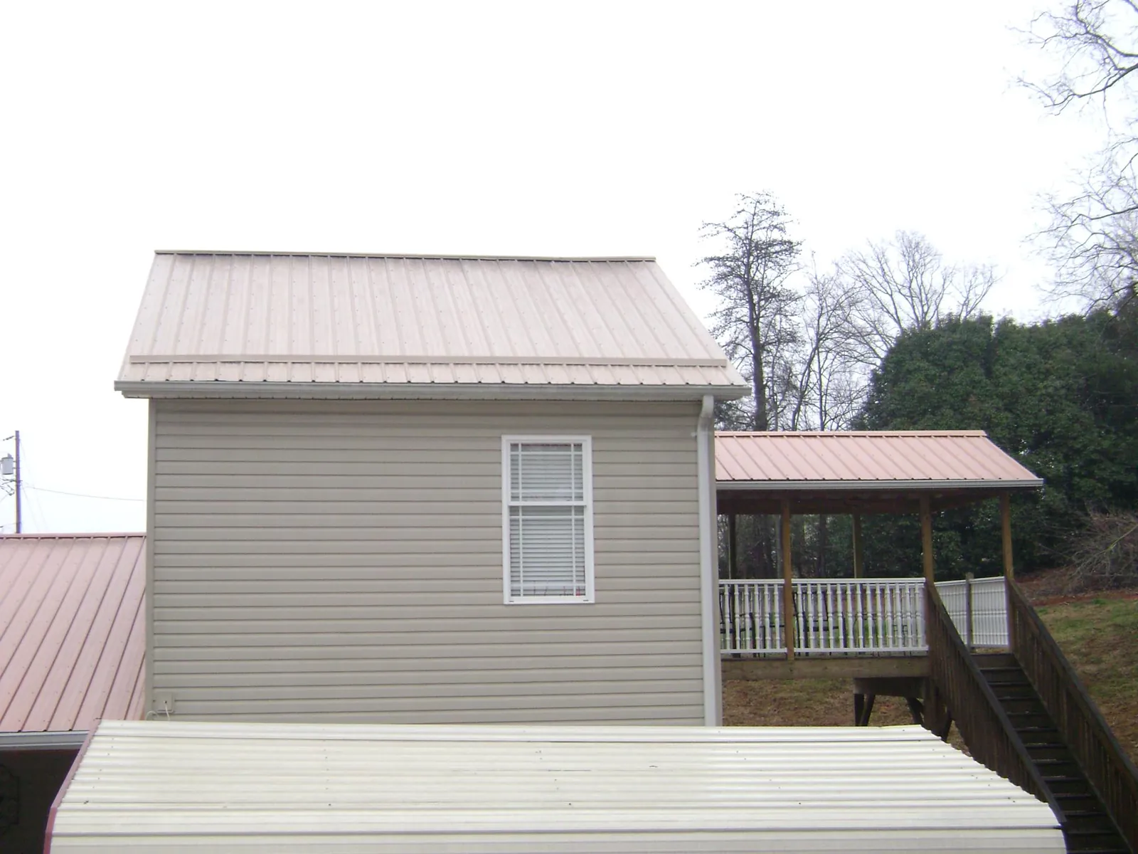 Tan metal roofs on a two story addition and attached porch, from a Roof Replacement job in Blue Rock
